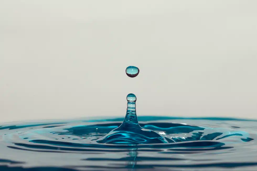 Photographie d'une goutte d'eau bleue tombant dans un flaque d'eau